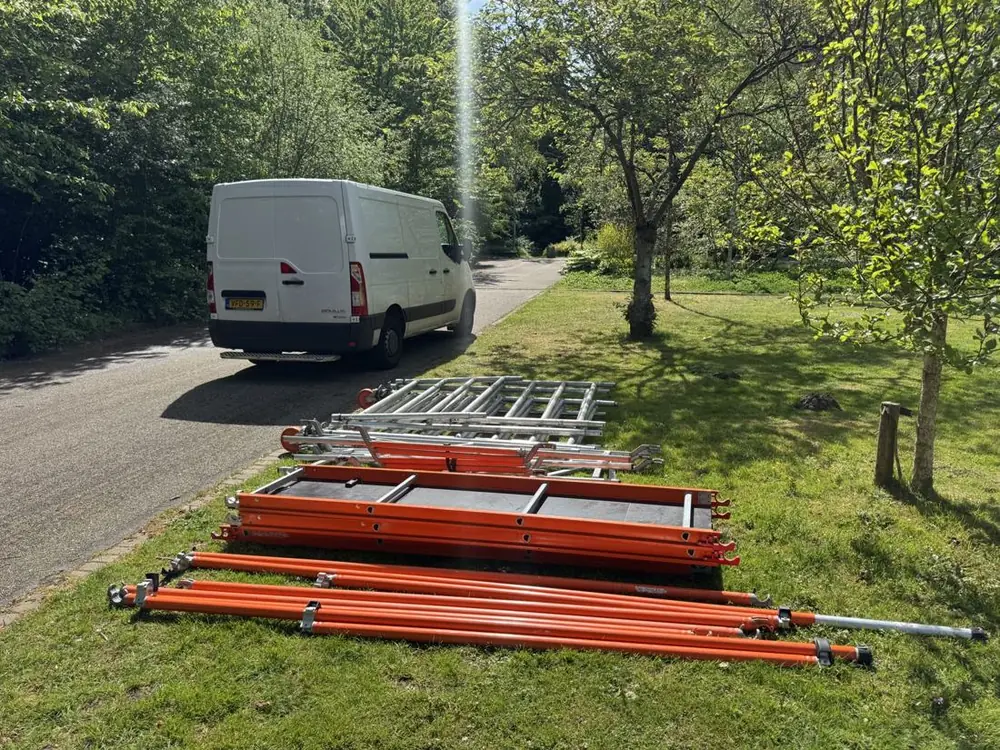 Uitgeladen rolsteigeronderdelen in het gras, met de bezorgbus op de achtergrond