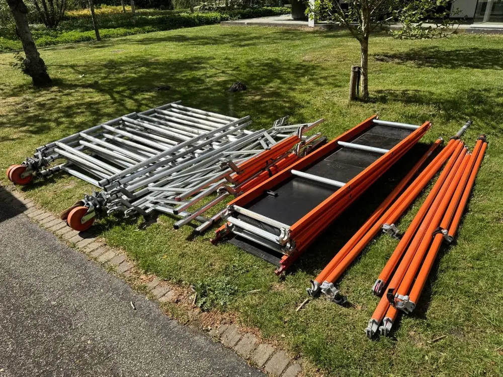 Alle onderdelen van een rolsteiger uitgelegd op het gras: frames, platformen, schoren en wielen