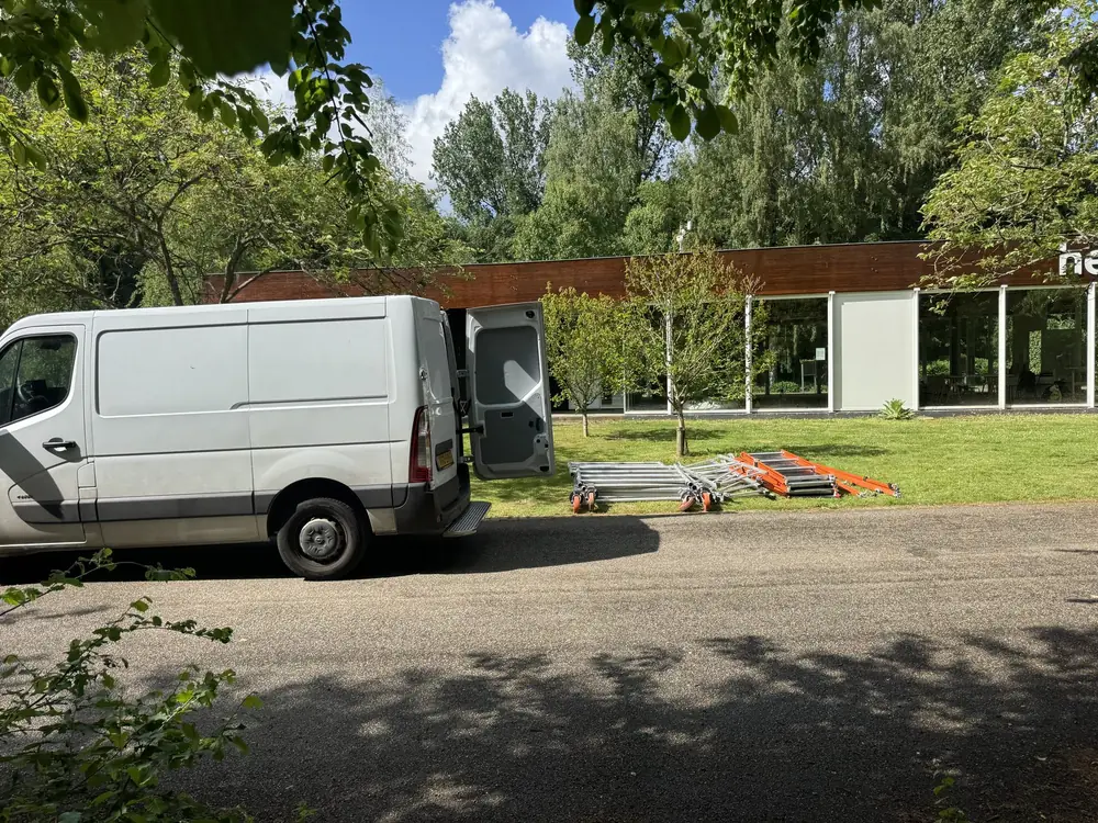 Bus van Steigertaxi die steigerdelen bezorgt bij een woning, ruim voor de dag waarop de kraan komt