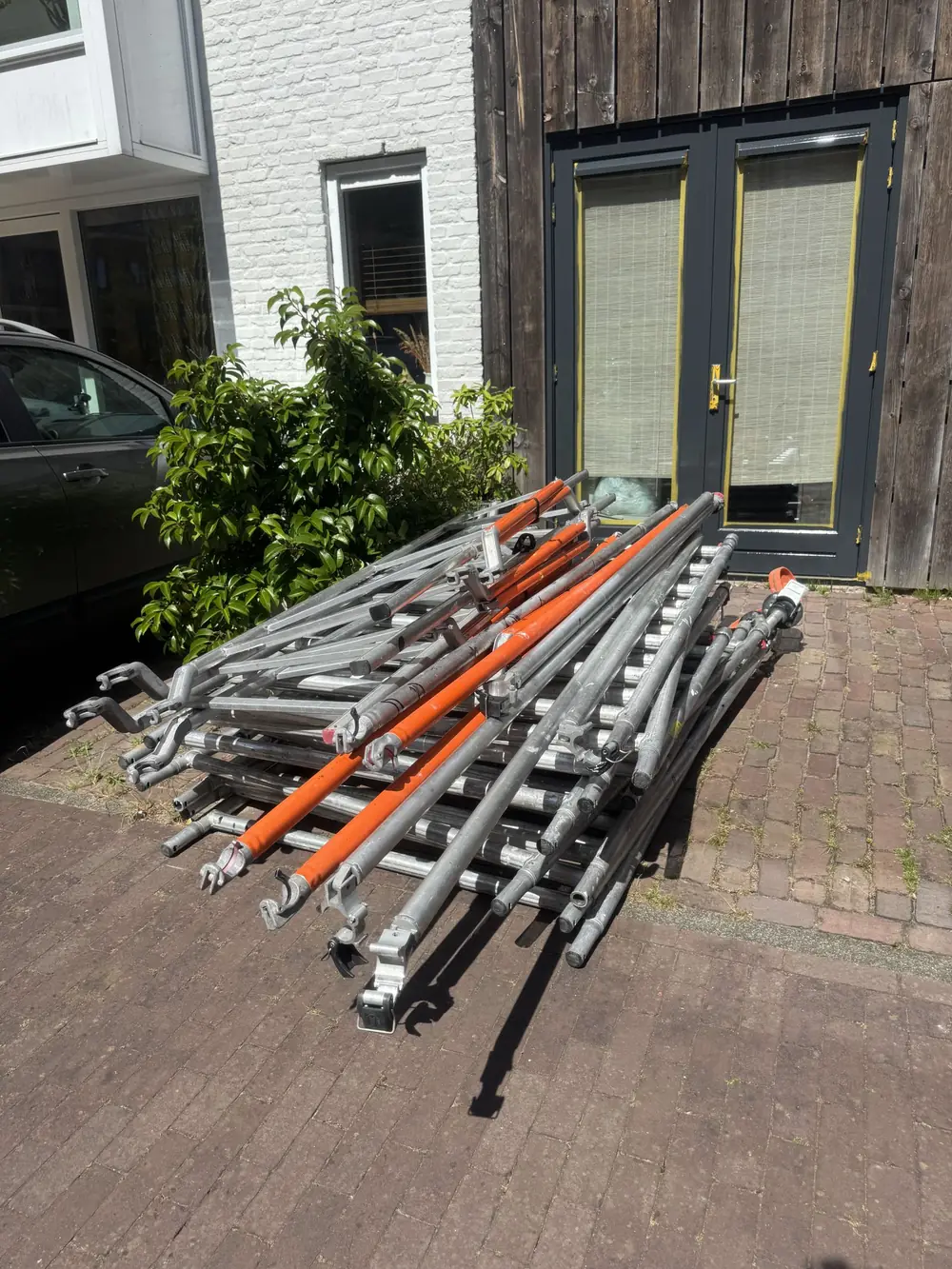Losse frames, oranje schoren en buizen op de oprit, samen de set waarmee je per standplaats 245 cm dek krijgt